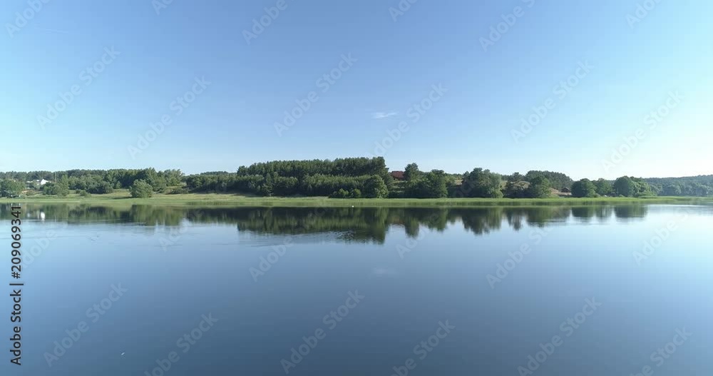 Fast establishing shot from over lake surface over tree tops revealing rural European countryside Fast establishing shot from over lake surface over tree tops revealing rural European countryside