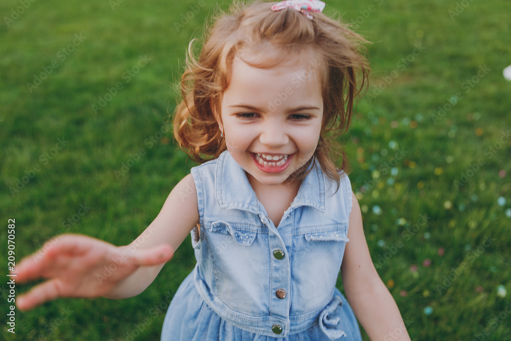 Smiling little cute child baby girl in denim dress pointing hand on camera, have fun on green grass lawn in park. Mother, little kid daughter. Mother's Day, love family, parenthood, childhood concept. Smiling little cute child baby girl in denim dress pointing hand on camera, have fun on green grass lawn in park. Mother, little kid daughter. Mother's Day, love family, parenthood, childhood concept.