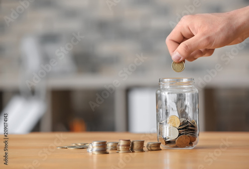 Man putting coins into glass jar on table. Savings concept