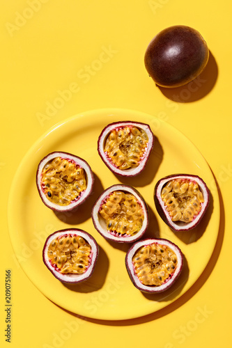 Whole and halved purple passion fruit, on a plate, casting shadows on a yellow background.