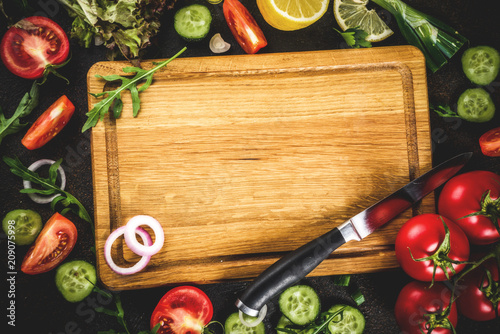 Cooking background, fresh salad ingredients, italian cuisine - tomatoes, olive oil, lemon, cucumbers, arugula, parsley, onions, with knife and cutting board, Dark rusty background copy space top view