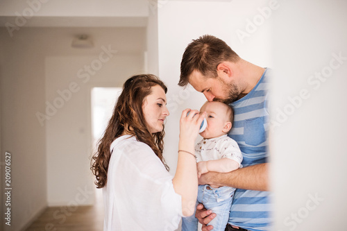 Young family with a baby boy drinking from a plastic bottle at home.