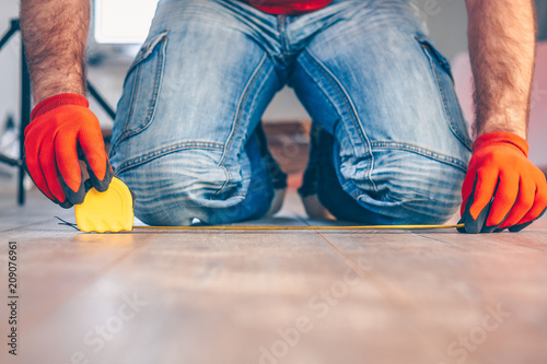 A worker with a construction measuring tape makes measurements on a wooden floor