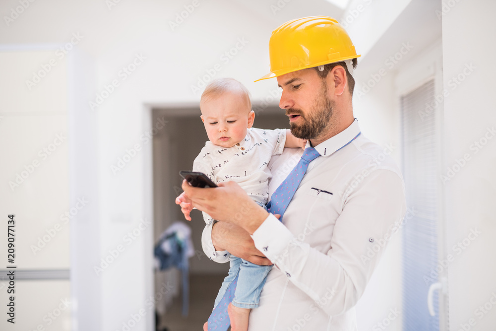 Father with shirt, tie, helmet and smartphone holding a baby son at home. Father with shirt, tie, helmet and smartphone holding a baby son at home.