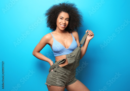 Beautiful African-American woman in bikini and jumpsuit on color background