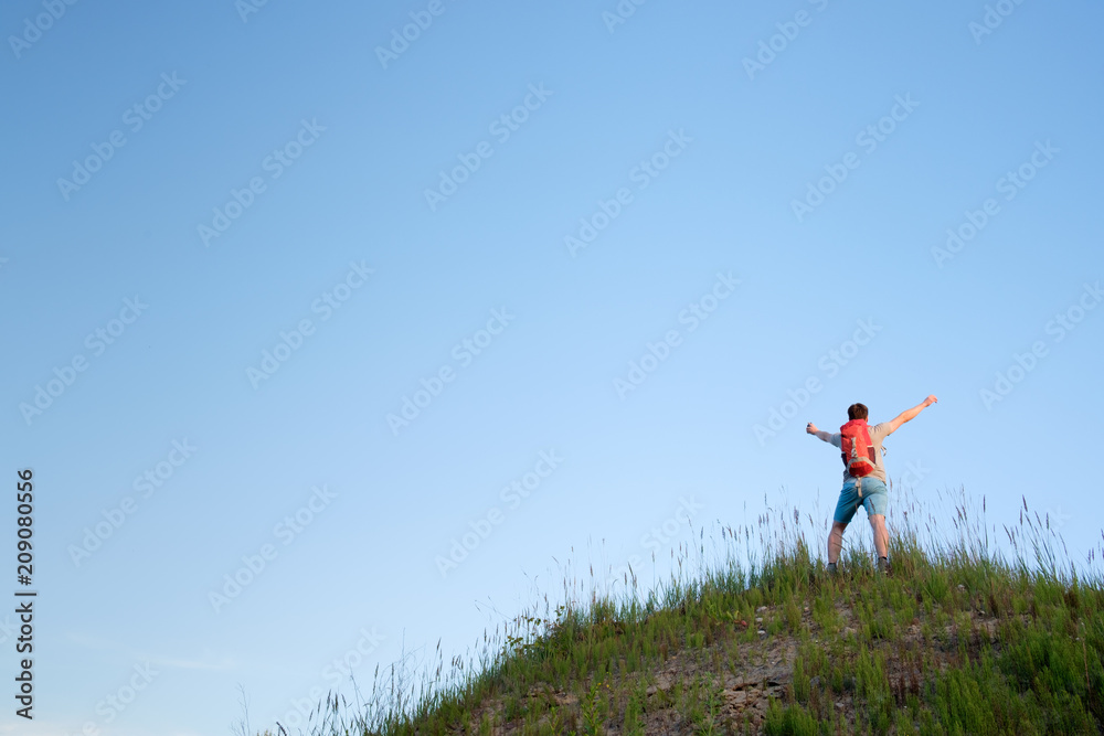 traveler with orange backpack hiking in the hills on blue sky background, view from behind traveler with orange backpack hiking in the hills on blue sky background, view from behind