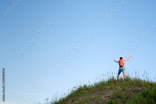 traveler with orange backpack hiking in the hills on blue sky background, view from behind