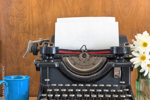 Vintage typewriter scene with a coffee cup & white flowers. Black antique typewriter with blank sheet of paper. Business concept of writing, typing, memo, letter, author