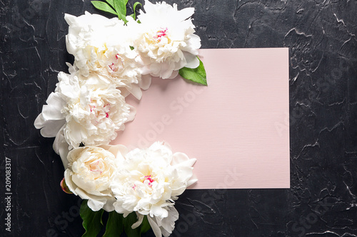 Beautiful peony flowers with blank card on dark textured background