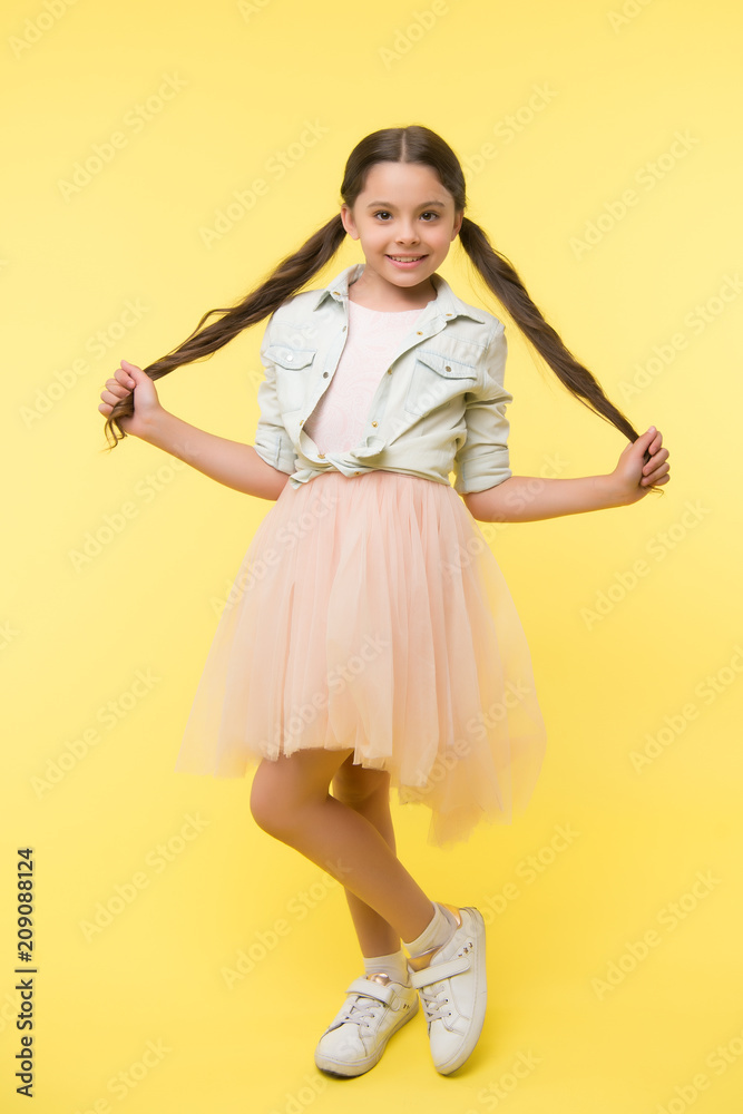 Check out my style. Kid girl charming ponytail hairstyle cute happy yellow  background. Child fashionable outfit skirt and denim jacket. Kid stylish  fashionable posing holds her long curly hair Stock Photo |