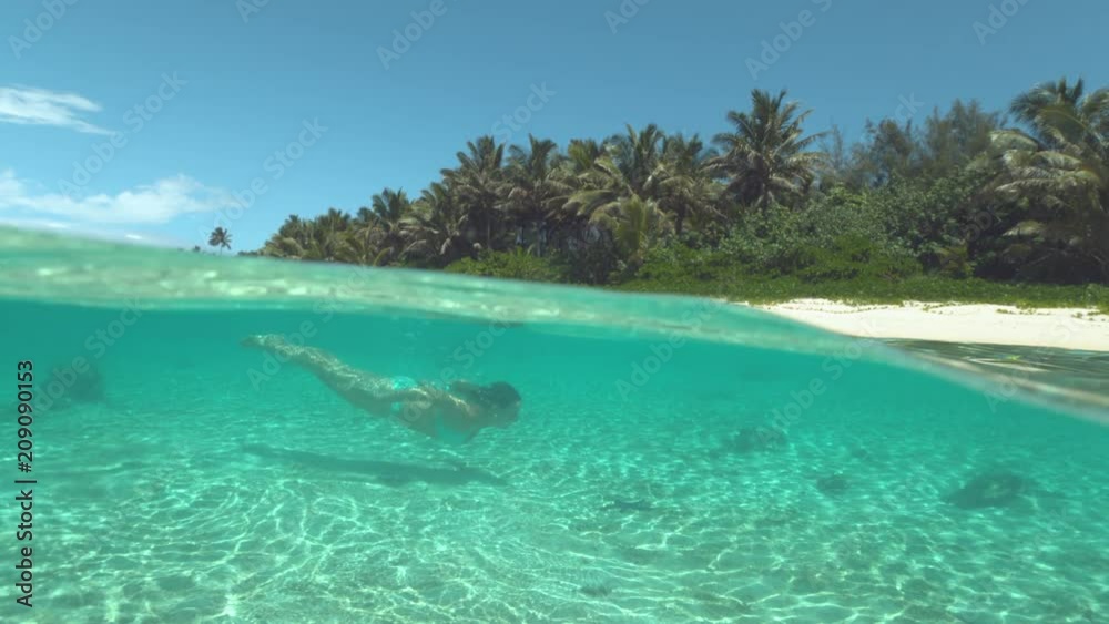 SLOW MOTION, HALF UNDERWATER: Active girl on vacation dives past dark starfish sitting on the sandy ocean floor. Young woman in turquoise bikini swims underwater close to the amazing white sand beach. SLOW MOTION, HALF UNDERWATER: Active girl on vacation dives past dark starfish sitting on the sandy ocean floor. Young woman in turquoise bikini swims underwater close to the amazing white sand beach.