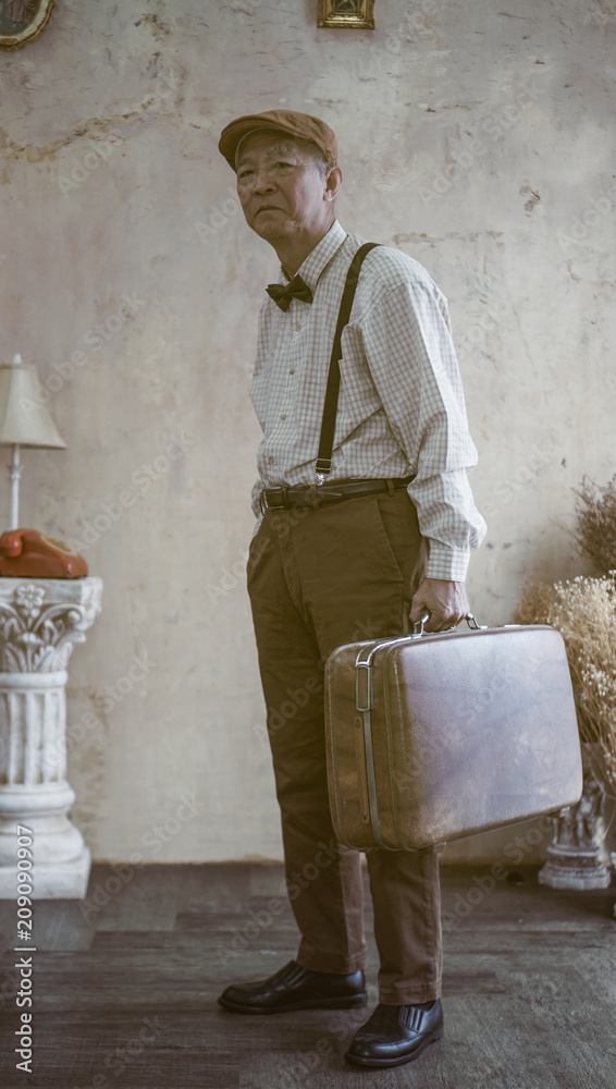 Φωτογραφία Retro vintage fashion Asian senior man wear flat cap and suspender carry luggage