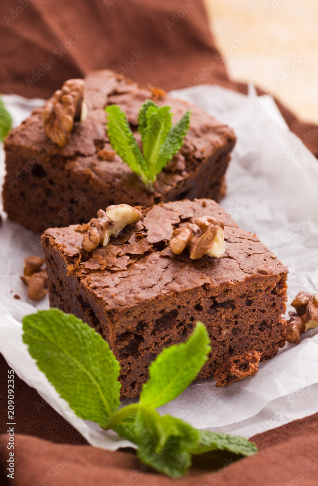 Brownie sweet chocolate dessert with walnuts and meant leaves on white paper with copy space on pastel beige background.