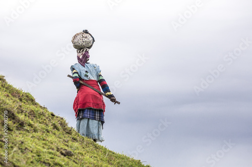 Native black African woman carries a load on her head in the hills of South Africa photo