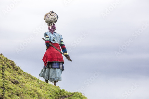 Native black African woman carries a load on her head in the hills of South Africa photo