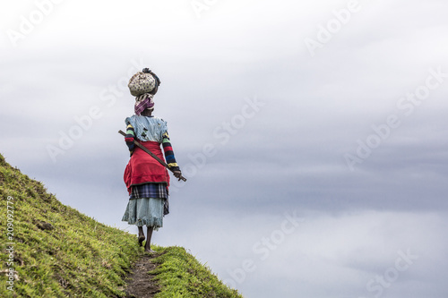 Native black African woman carries a load on her head in the hills of South Africa photo