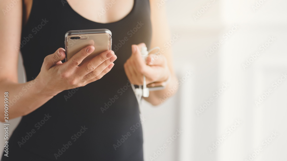 Closeup of slim woman in sportswear holding smartphone and earphones Closeup of slim woman in sportswear holding smartphone and earphones