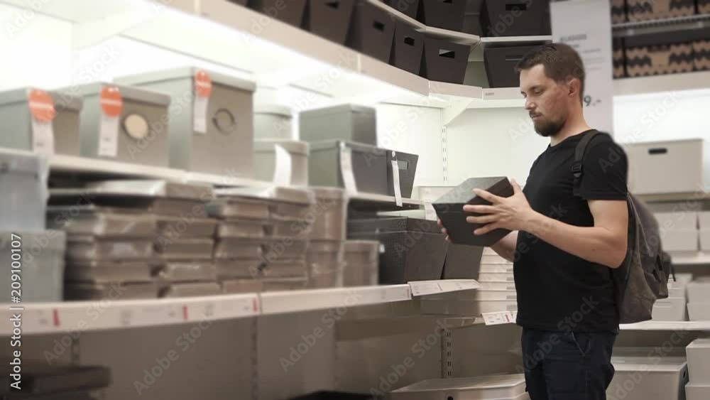 Adult male shopper is taking carton box from rack and holding in hands, deciding to buy. He is walking over sales area and looking for necessary goods Adult male shopper is taking carton box from rack and holding in hands, deciding to buy. He is walking over sales area and looking for necessary goods