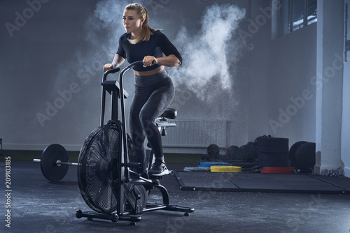 Athletic woman doing air bike workout at gym photo