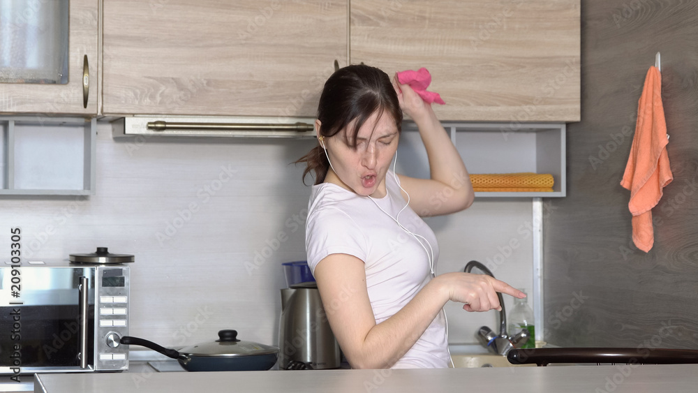 Beautiful woman is cleaning in the kitchen, dancing to the music in the headphones Beautiful woman is cleaning in the kitchen, dancing to the music in the headphones