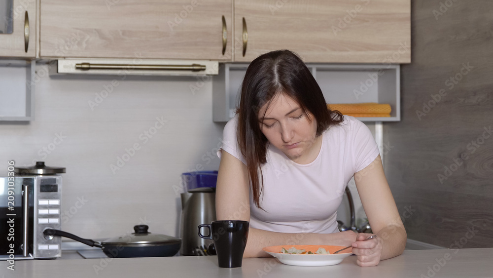 Young woman, falling asleep, eating at the table in the kitchen Young woman, falling asleep, eating at the table in the kitchen