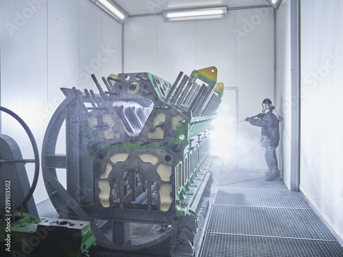 Worker cleaning engine block in washing bay
