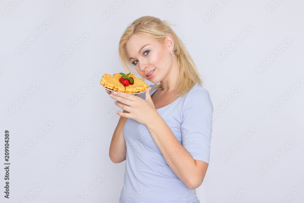 A happy blonde is holding a plate with Belgian waffles in her hands. Breakfast is decorated with strawberries and mint leaves. Concept: home food.