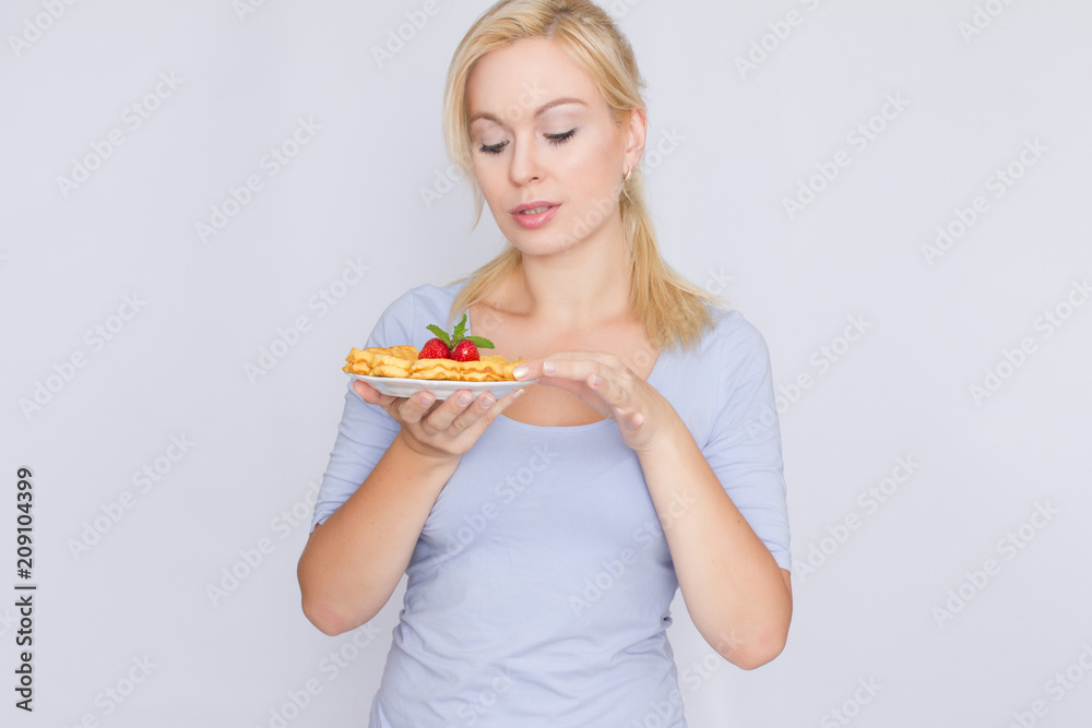 A happy blonde is holding a plate with Belgian waffles in her hands. Breakfast is decorated with strawberries and mint leaves. Concept: home food. A happy blonde is holding a plate with Belgian waffles in her hands. Breakfast is decorated with strawberries and mint leaves. Concept: home food.