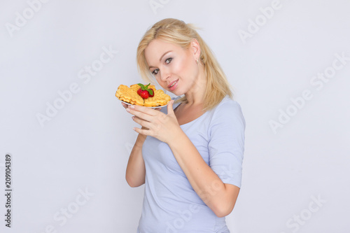 A happy blonde is holding a plate with Belgian waffles in her hands. Breakfast is decorated with strawberries and mint leaves. Concept  home food.