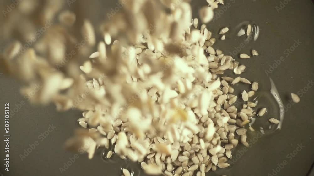 Peeled sunflower seeds do not pour into the oil in a gray bowl top view slow motion Peeled sunflower seeds do not pour into the oil in a gray bowl top view slow motion