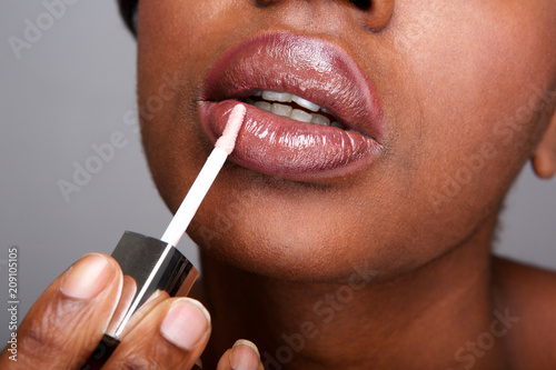 Close up beautiful african american woman applying shiny lip gloss photo