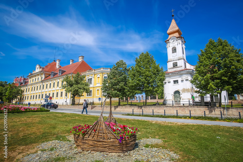 View of a large straw basket with flowers in a park with people walking in the street and the City museum and Chapel of the Saint Roko in the background in Vukovar, Croatia.
