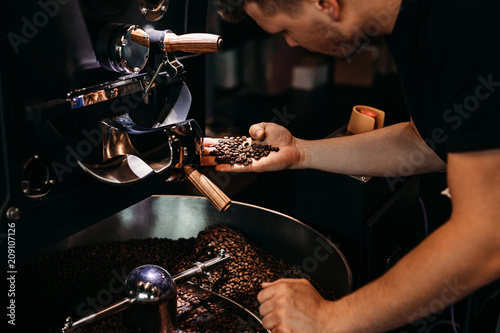 Man working at coffee production. Barista controling coffee grounds roasting process. photo