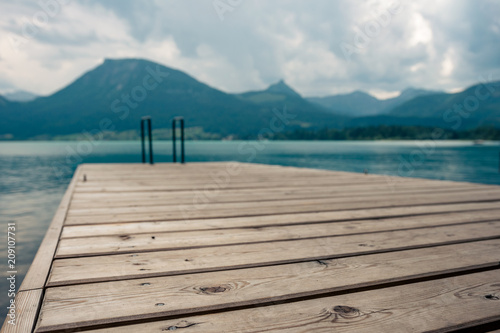 Leiter vom Steg in den klaren erfrischenden türkisen See namens Wolfgangsee in Österreich mit Berge im Hintergrund und Wolken am Himmel © Christian