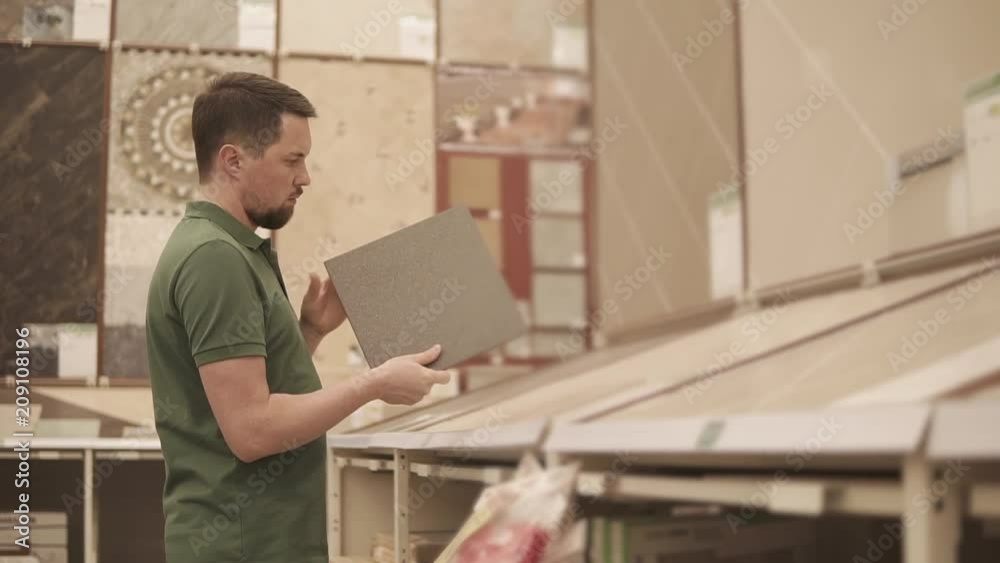Man is choosing ceramic lining in a big shop. He is taking one piece from rack and looking, rotating it in hands Man is choosing ceramic lining in a big shop. He is taking one piece from rack and looking, rotating it in hands