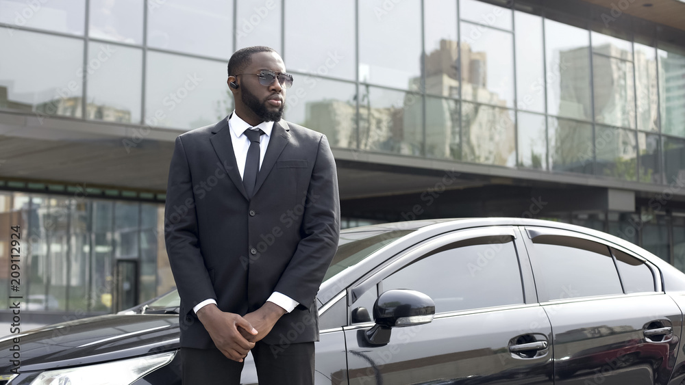 Confident Afro-American driver standing by car, security guard service, business Confident Afro-American driver standing by car, security guard service, business