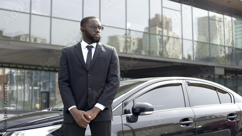 Confident Afro-American driver standing by car, security guard service, business © motortion
