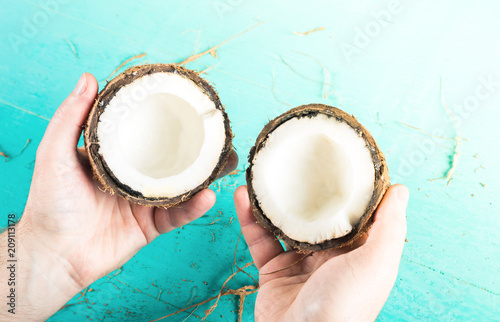 Two halves of chopped coconut in hands on a blue background with peel