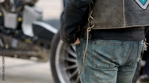 Tough biker with hands in jeans pockets standing next to his cool motorcycle