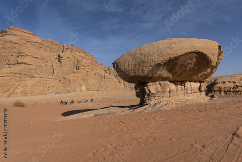 Mushroom rock and a group of people riding the horses background in Wadi Rum Desert, Jordan