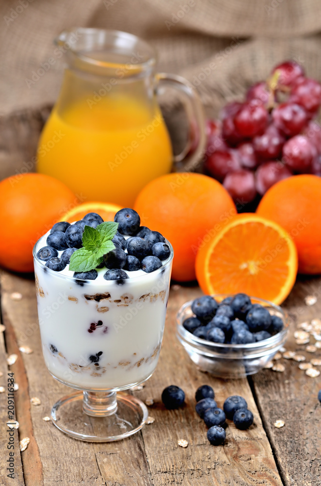 Greek yogurt with oatmeal, fresh blueberries, mint and orange juice, grapes in background vertical photo Greek yogurt with oatmeal, fresh blueberries, mint and orange juice, grapes in background vertical photo