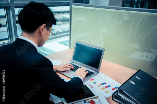 Asian businessman in black suit think idea for work at office,he work overtime alone in a company,dark tone,stress man work on laptop