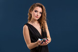 Elegant female casino player holding a handful of chips on dark blue background. Copy space