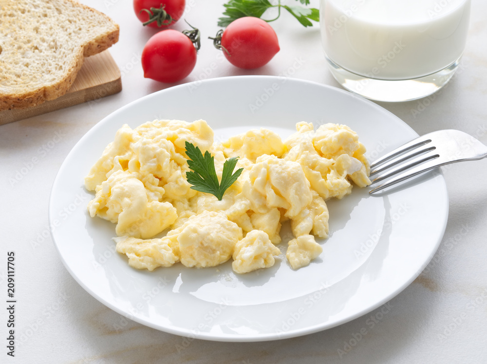 white plate with pan-fried scrambled eggs on a white light background with tomatoes. Omelette, side view