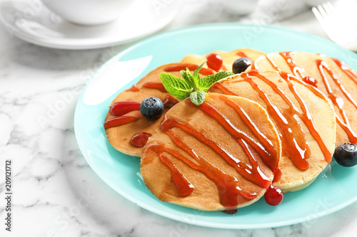 Tasty pancakes with berries and syrup on table
