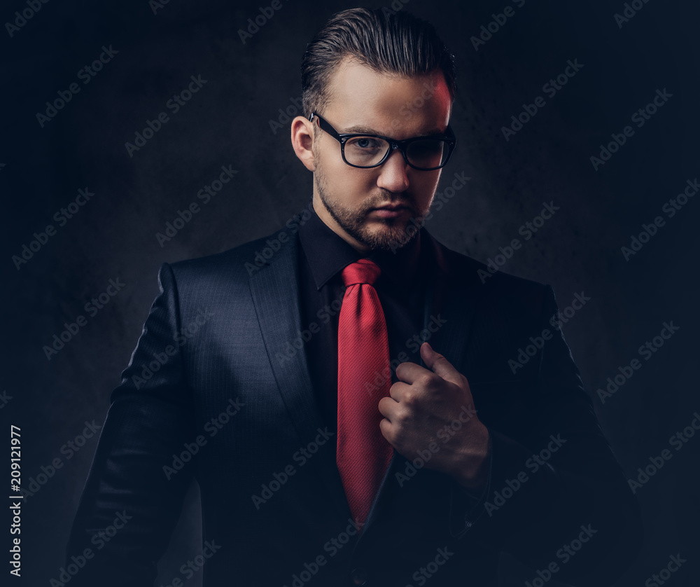 Portrait of mystical stylish male in a black suit and red tie. Isolated on a dark Stock Adobe Stock