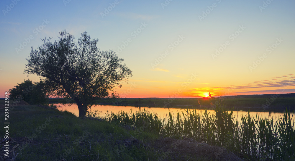 Beautiful colorful sunset on the bankk of river.Summer serene landscape.