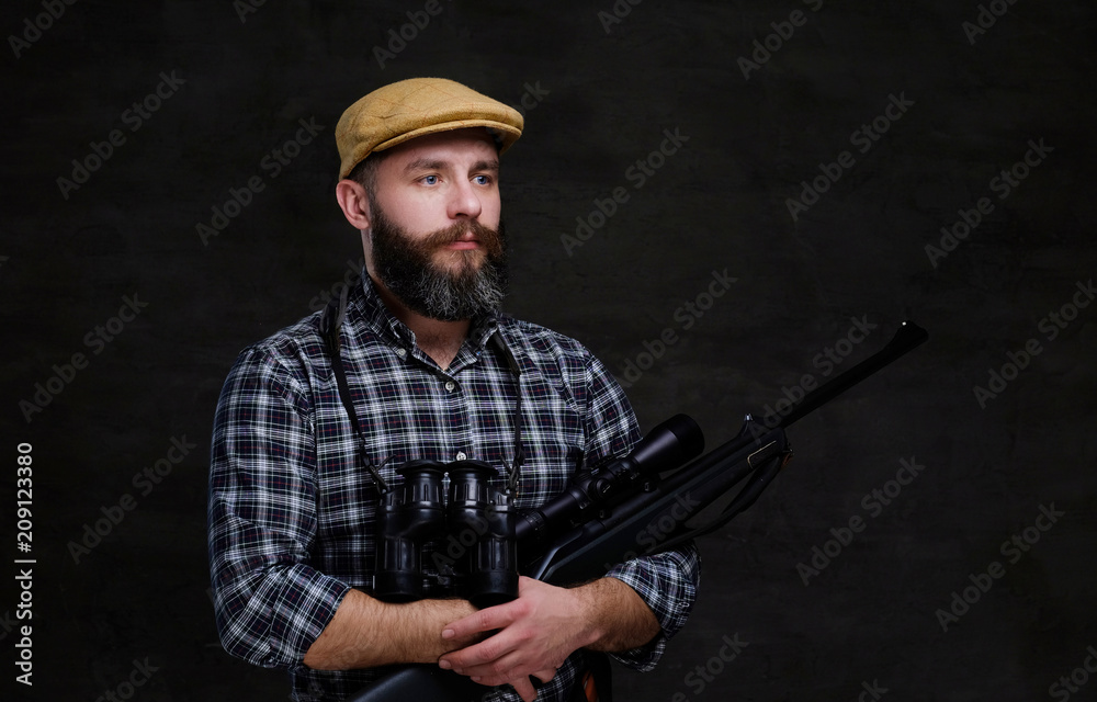 Portrait of a bearded hunter traveler in a fleece shirt and hat holds rifle with a sight and binoculars. Portrait of a bearded hunter traveler in a fleece shirt and hat holds rifle with a sight and binoculars.