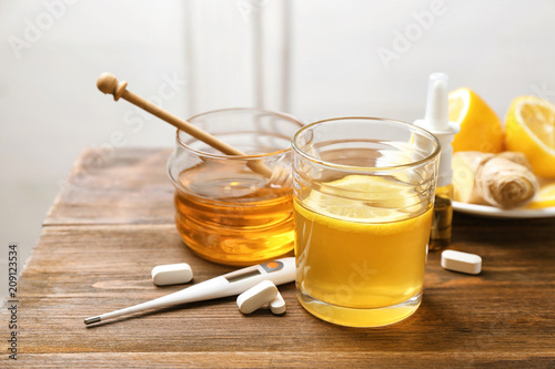 Glass with hot tea, honey and pills for cold on wooden table