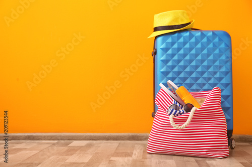 Suitcase and bag packed for summer journey on floor near color wall